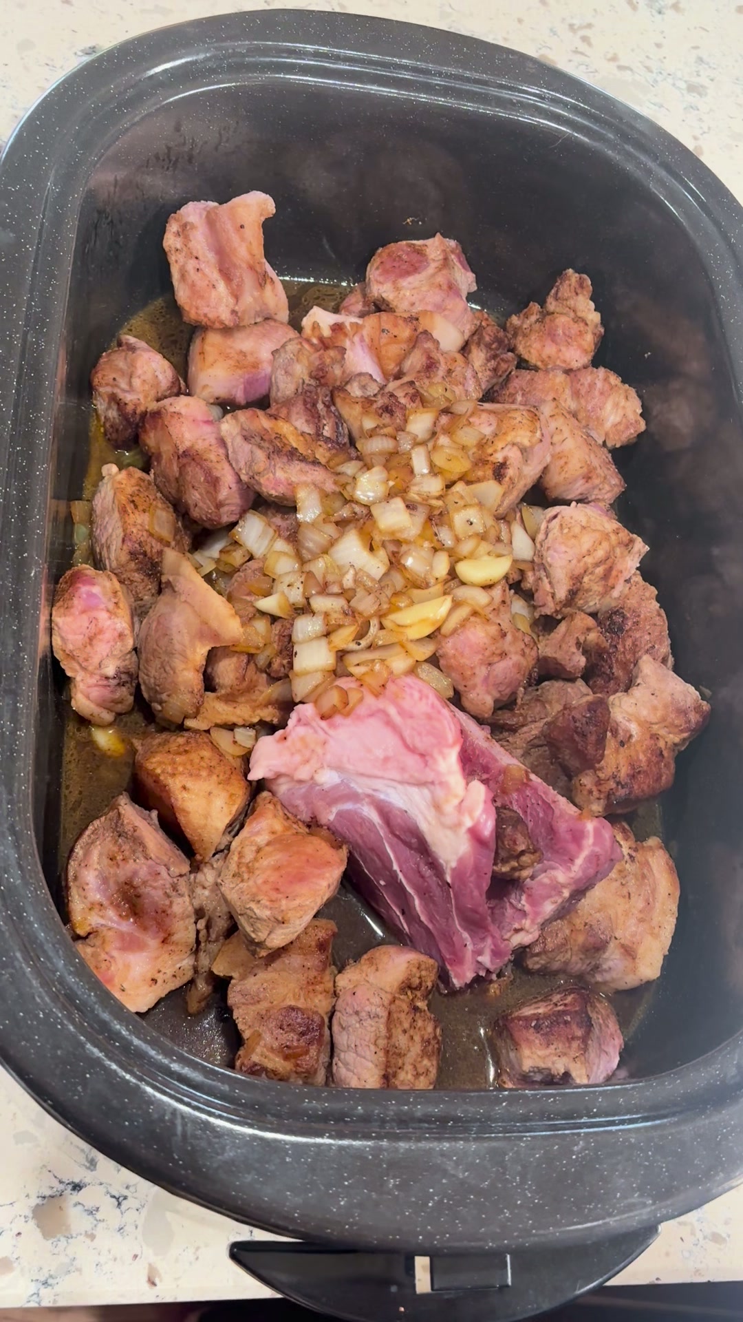 Seared cubed pork shoulder in the roaster with caramelized onions and garlic in the center