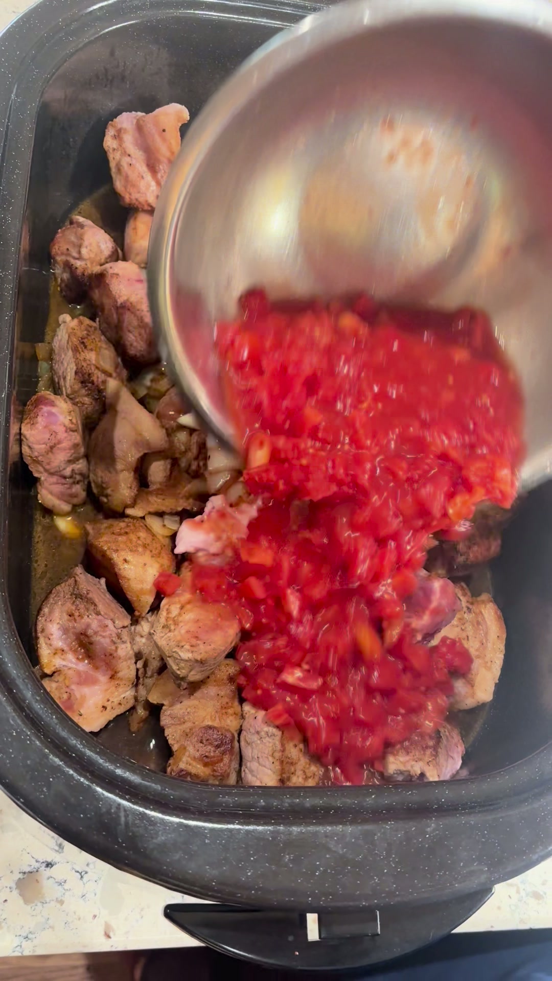 Diced tomatoes cascading from a stainless bowl onto the seared pork