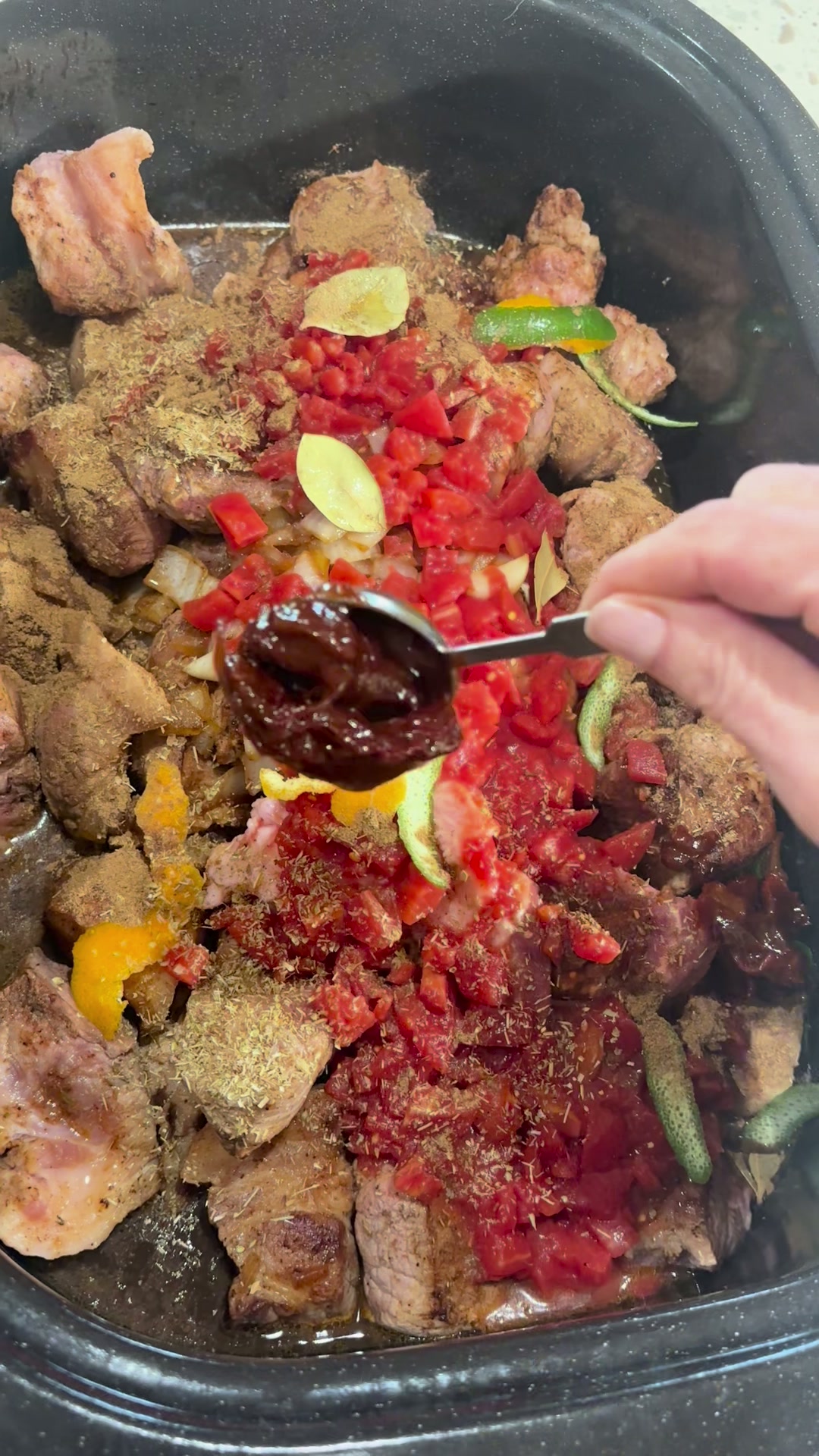 A measuring spoon holding a whole glossy chipotle in adobo over the pot
